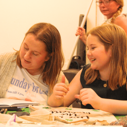 Photo of a woman and a child smiling and writing and drawing