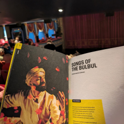 A photo of a performance programme that has a photo of a man dancing with rose petals and the words 'songs of the bulbul'