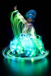 A south Asian man, dressed in blue and white dances, neon light swirls around him