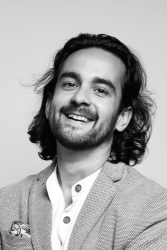 A black and white headshot of a Scottish Indian man looking at the camera