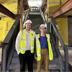 A man and a woman wearing a high vis jacket and a hard hard inside of a building site in front of some stairs