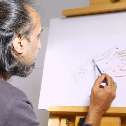 A photo of a man doing some calligraphy with blue ink on a white piece of paper on an easel