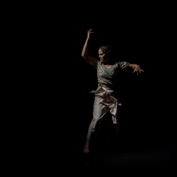 A woman dancing dressed in white on a black stage