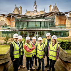 A group of people wearing high vis jackets and hard hats in front of a glass building