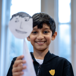 A photo of a little boy holding up a paper puppet