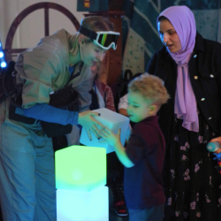 A photo of a little boy and two women stacking light up cubes