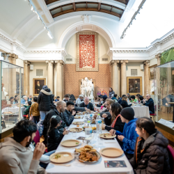 A group of people on a long table all sharing an Iftar meal inside of a museum