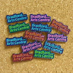 A selection of badges in blue, orange, green and pink, all reading 'Bradford Arts Centre'