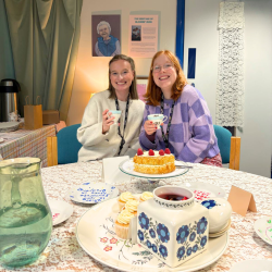 A photo of two girls holding tea cups and eating cake in a vintage tea room