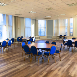 A photo of tables and chairs in a large hall with big windows