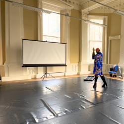 A dancer in high heels and a kimono striking a post in a large hall